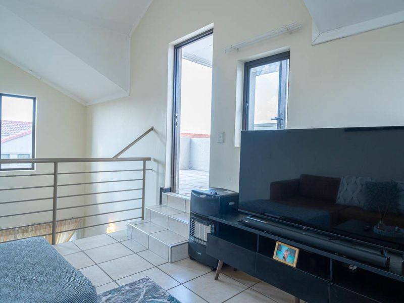 A living area featuring tiled flooring, a vaulted ceiling, and a metal balustrade, with direct access to an outdoor balcony area.
