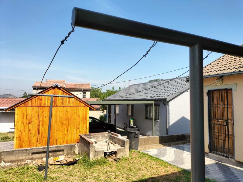 Rear garden area featuring a built-in braai, paved walkway, and access to the main dwelling and wooden outbuilding.