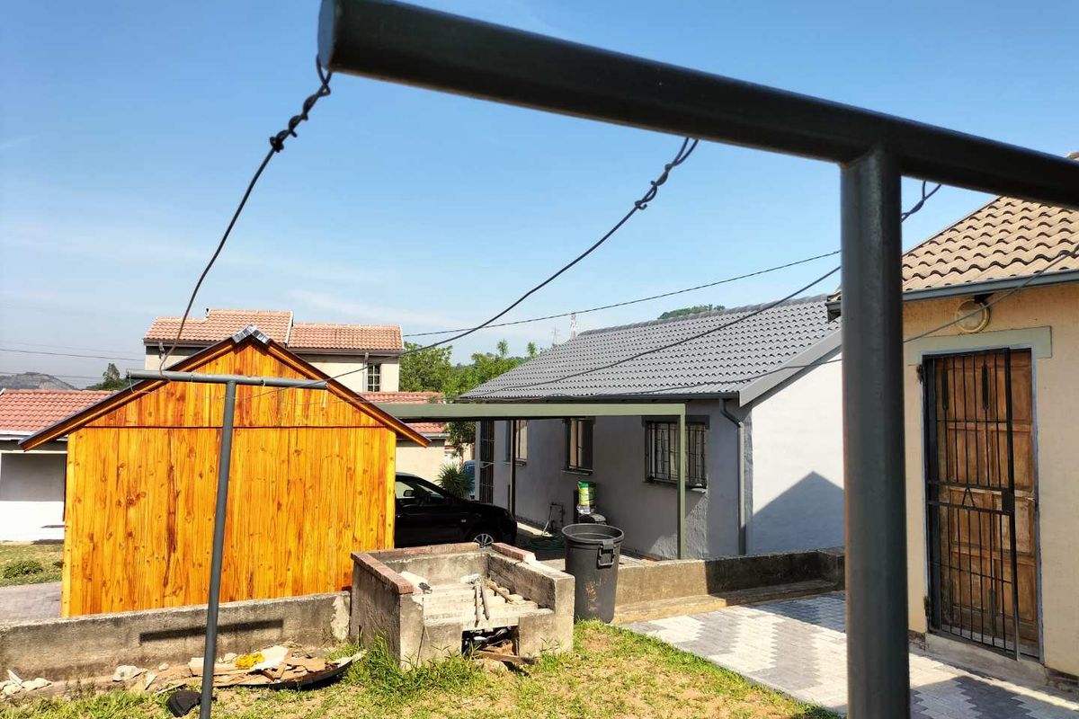 Rear garden area featuring a built-in braai, paved walkway, and access to the main dwelling and wooden outbuilding.