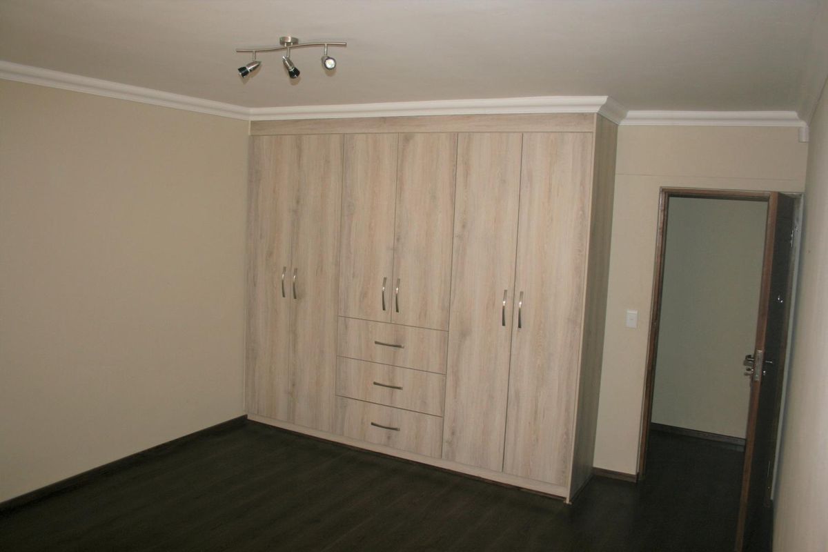 A bedroom featuring modern light wood-grain built-in cupboards with integrated drawers and dark laminate flooring.