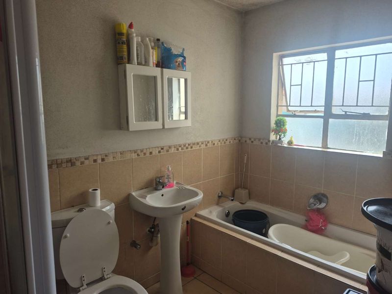 A functional bathroom featuring a pedestal basin, toilet, and bathtub with tiled splashbacks and security bars on the window.
