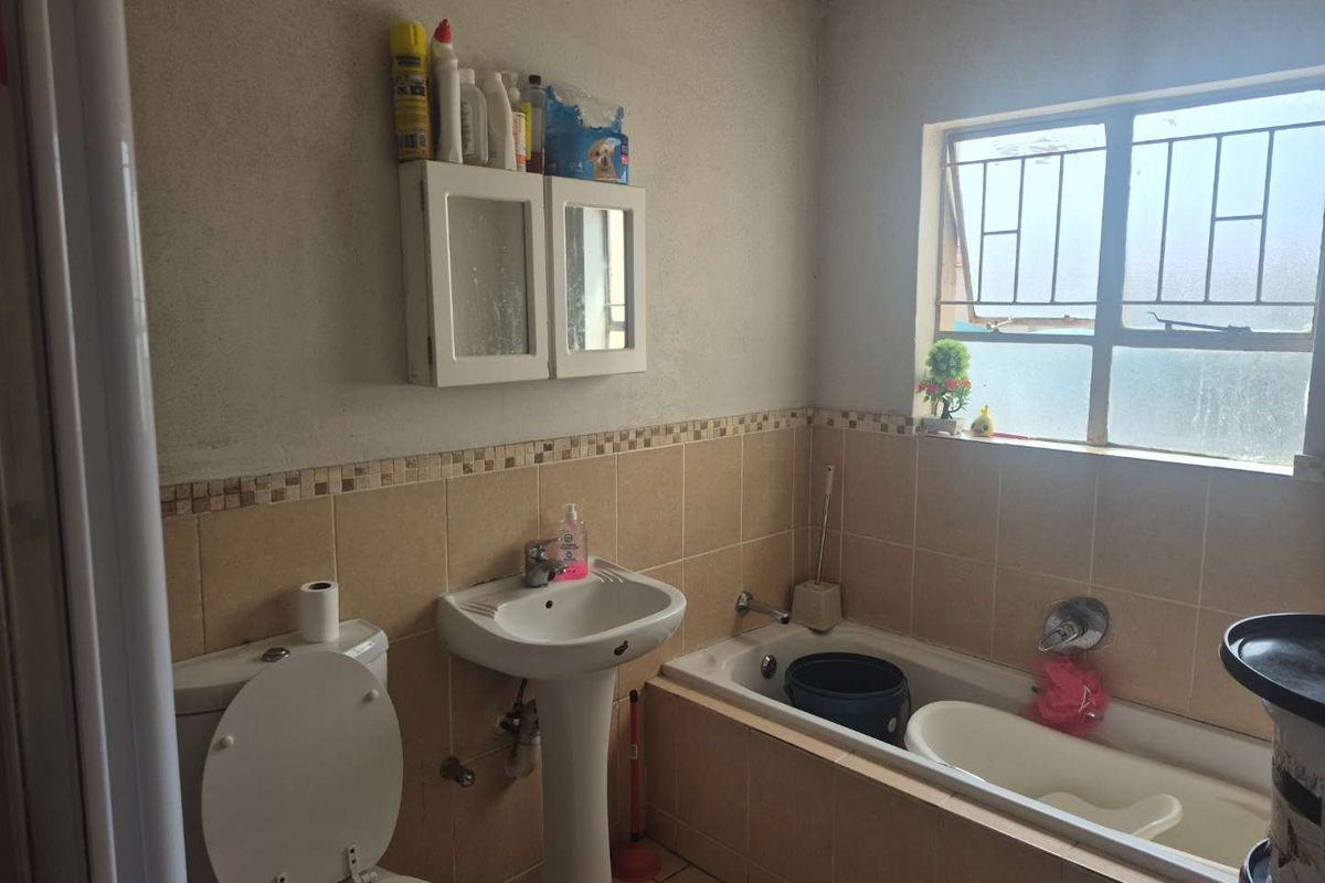 A functional bathroom featuring a pedestal basin, toilet, and bathtub with tiled splashbacks and security bars on the window.