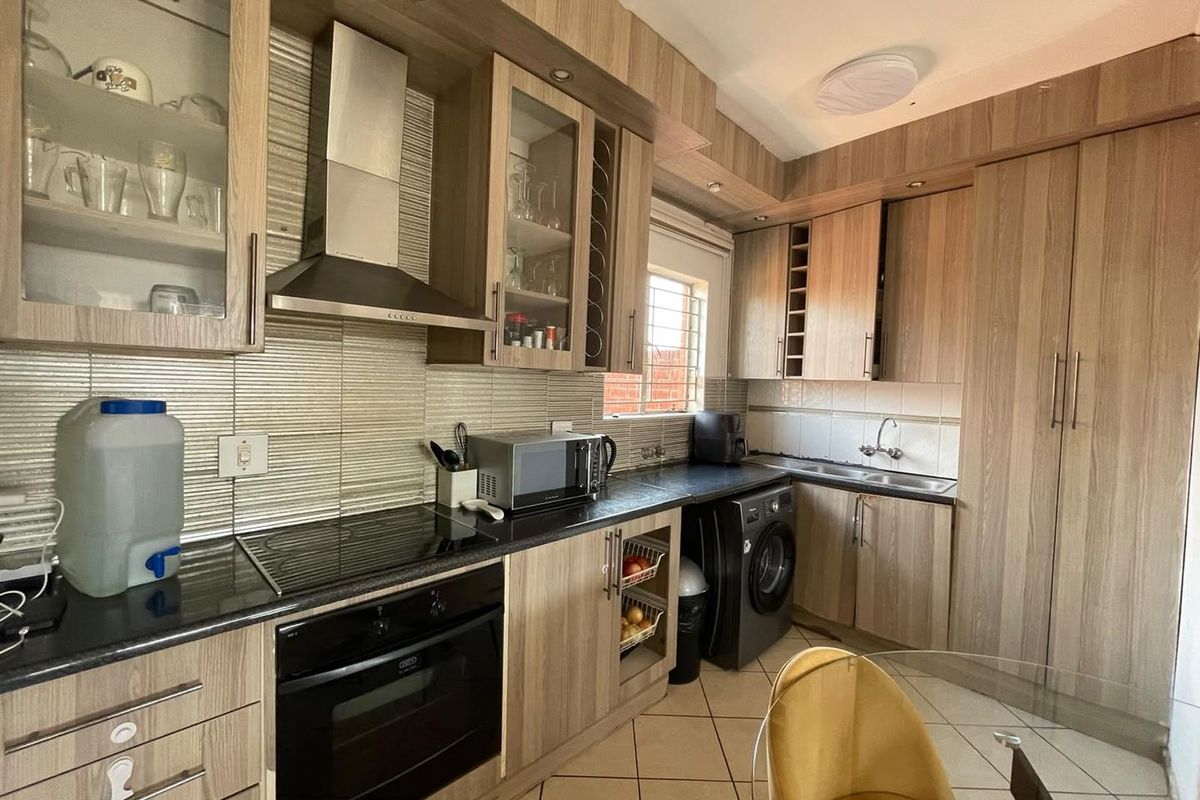 Functional kitchen featuring wood-look laminate cabinetry, built-in oven, electric hob, stainless steel extractor fan, and tiled backsplash with integrated laundry plumbing.
