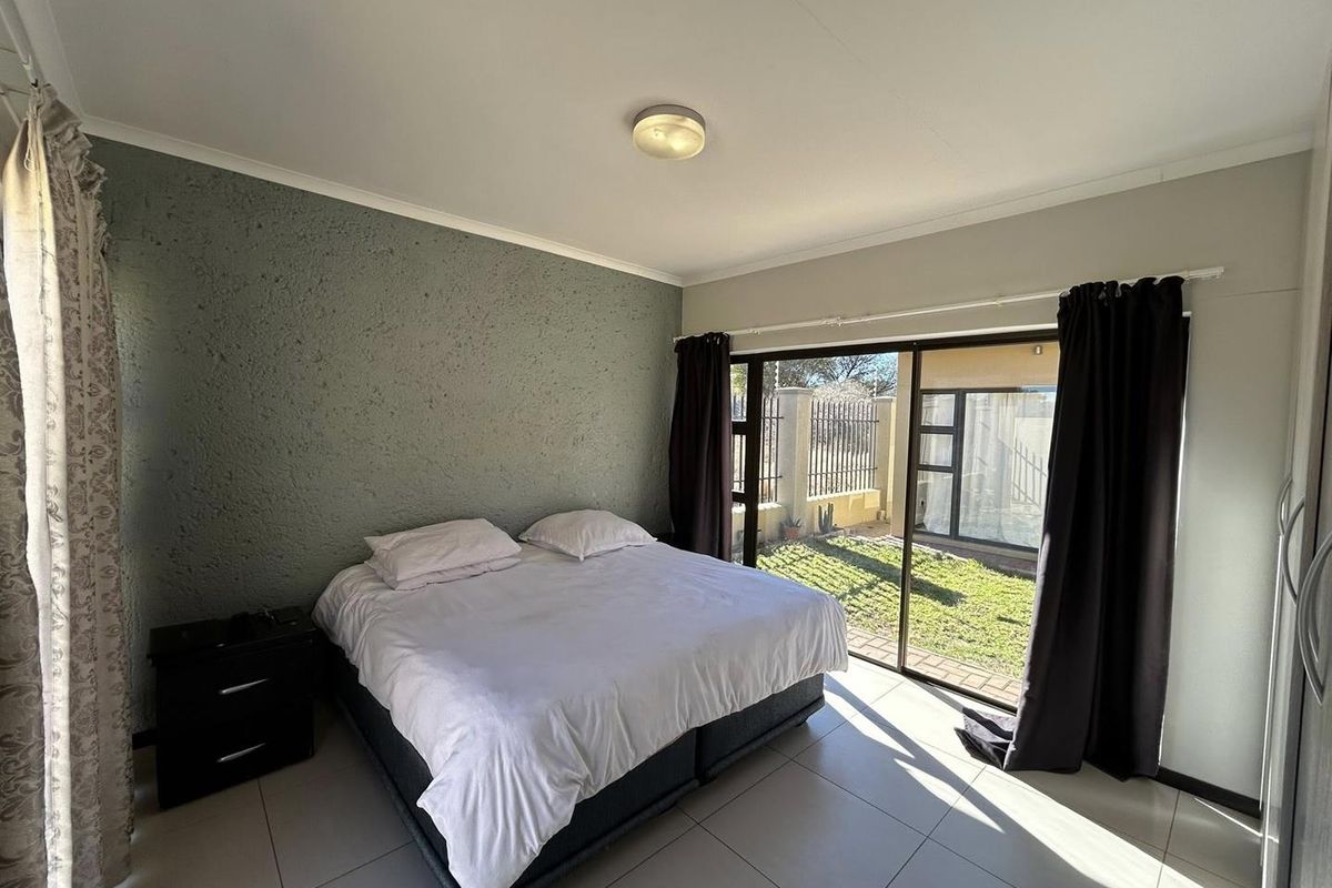 A bedroom featuring tiled flooring, a textured accent wall, and large sliding glass doors providing direct access to the rear garden area.
