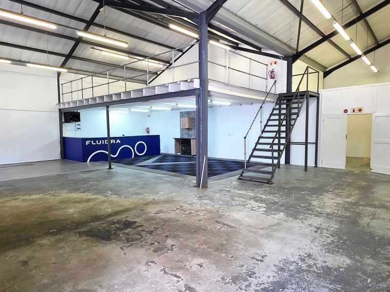 Spacious industrial open-plan warehouse featuring a mezzanine level, metal staircase, exposed steel trusses, and durable concrete flooring.