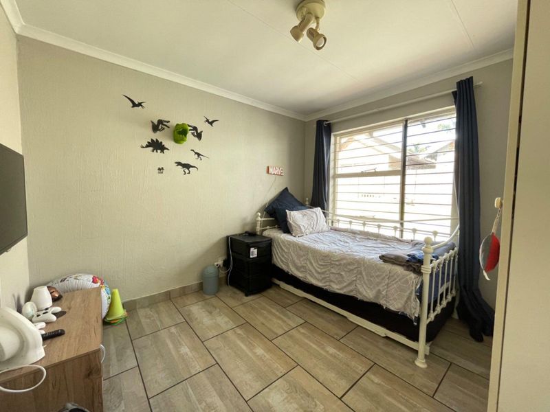 A bedroom featuring tiled flooring, a window with security bars, and a ceiling-mounted spotlight fixture.