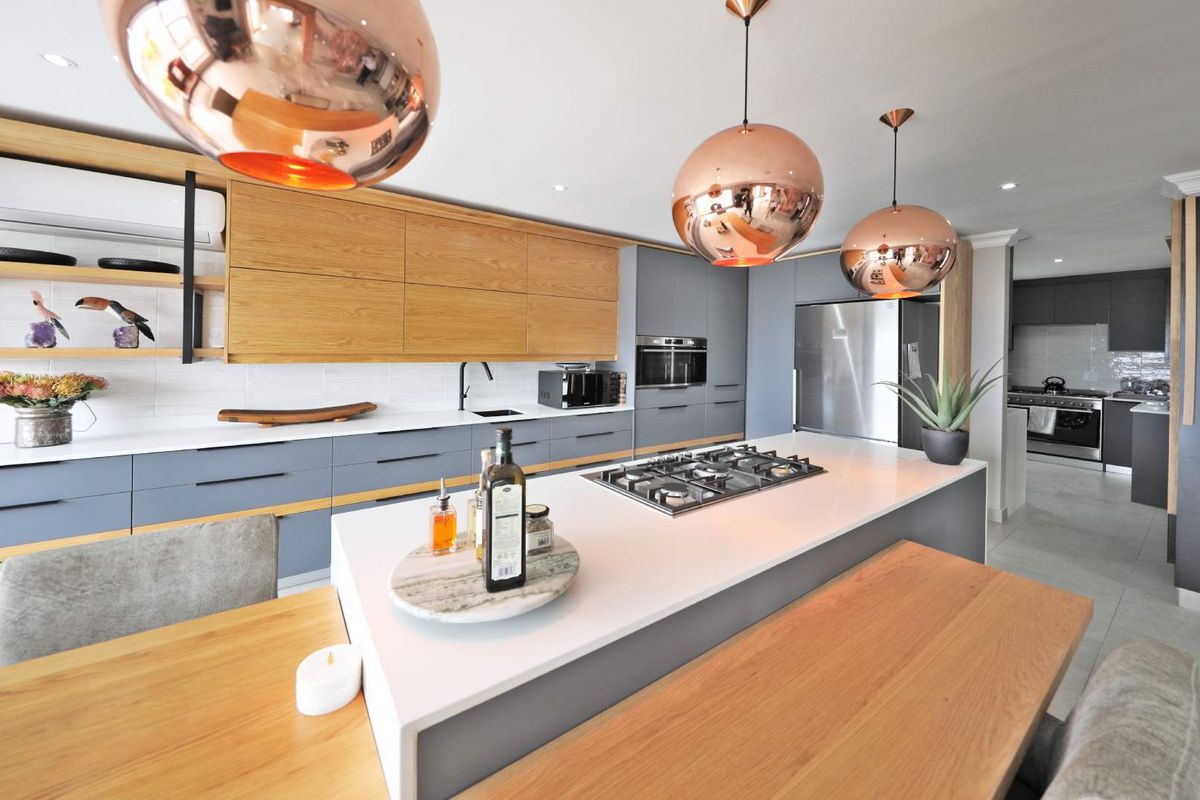 Modern kitchen featuring a central island with a built-in gas hob, sleek cabinetry, stone countertops, and integrated appliances, flowing into a secondary scullery area.