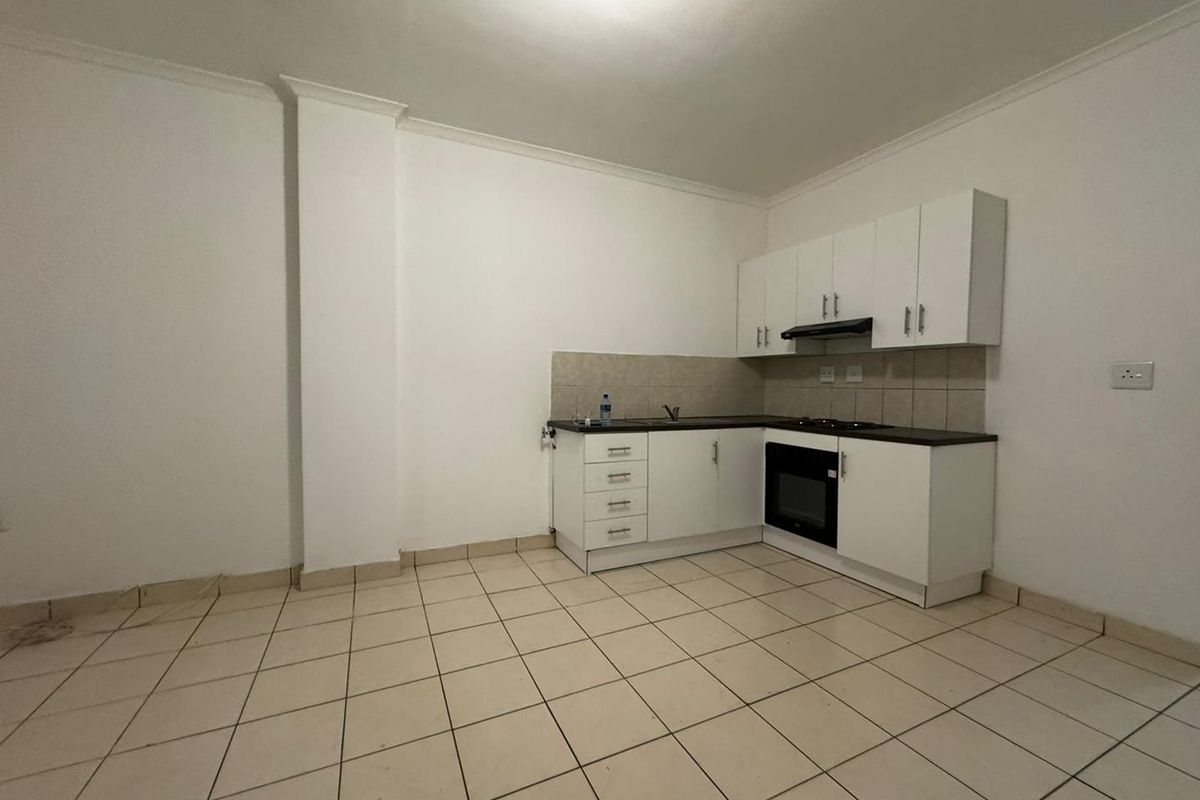 A compact, empty kitchen featuring white cabinetry, a built-in oven, extractor fan, and tiled flooring, offering a functional space ready for personalization.