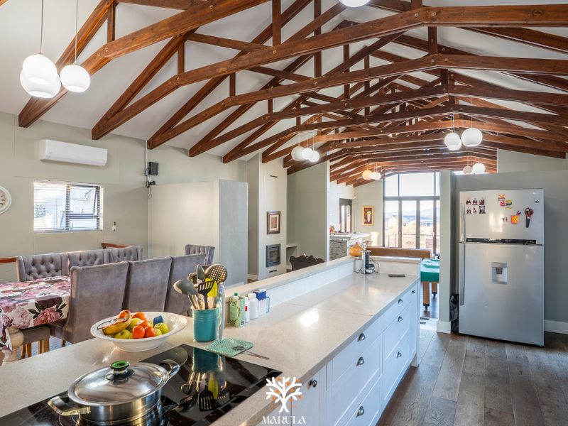Spacious open-plan living and kitchen area featuring high vaulted ceilings with exposed timber trusses, modern stone countertops, and integrated kitchen appliances.