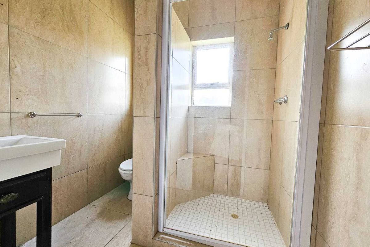 A compact bathroom featuring floor-to-ceiling beige tiling, a corner shower enclosure with a built-in seat, and a wall-mounted vanity basin.