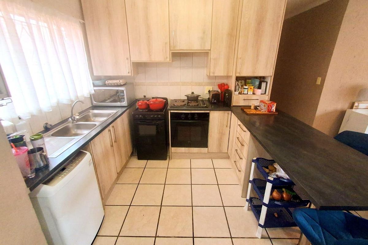Functional kitchen featuring light wood-look cabinetry, dark countertops, a built-in oven with hob, and tiled flooring with a breakfast bar area.