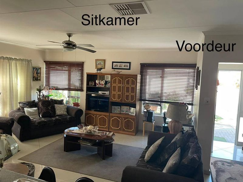 A living room area featuring tiled flooring, a ceiling fan, and venetian blinds, with direct access to the front entrance.