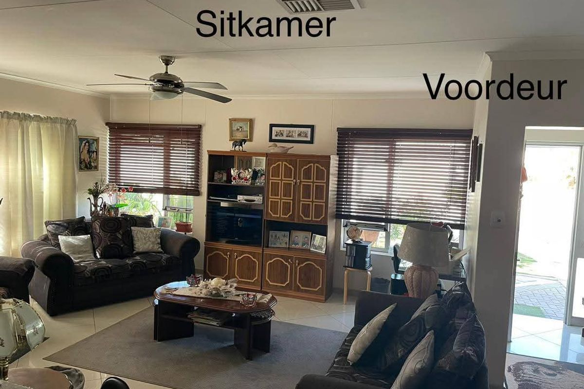 A living room area featuring tiled flooring, a ceiling fan, and venetian blinds, with direct access to the front entrance.