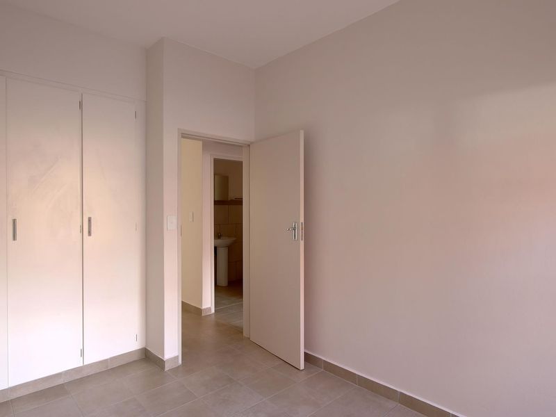 A clean, empty bedroom featuring neutral tiled flooring and built-in cupboards, with a doorway leading to an adjacent bathroom area.