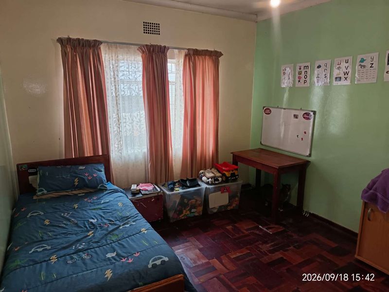A bedroom featuring traditional parquet flooring and a window with curtains, providing a functional space with potential for modernization.