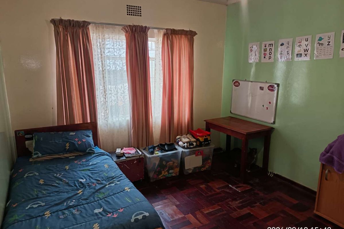 A bedroom featuring traditional parquet flooring and a window with curtains, providing a functional space with potential for modernization.