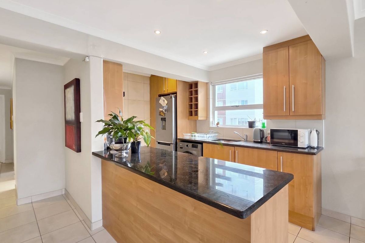 A functional kitchen featuring wooden cabinetry, granite countertops, a breakfast bar, and tiled flooring, illuminated by recessed downlights.