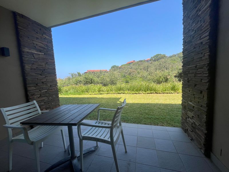 A covered patio featuring stone-clad pillars and tiled flooring, offering a direct view of the landscaped garden and surrounding hillside.