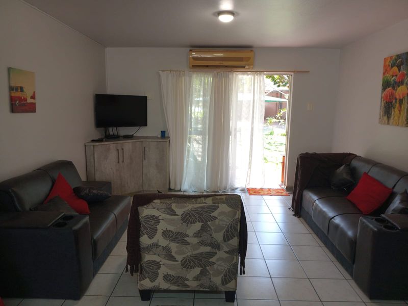 A living room featuring tiled flooring, a wall-mounted air conditioning unit, and a sliding glass door providing access to the outdoor area.