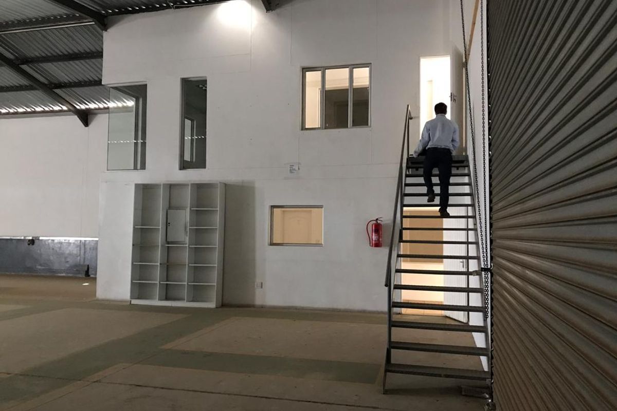 Industrial warehouse space featuring a mezzanine level with office access, metal staircase, roller shutter door, and exposed steel roof structure.