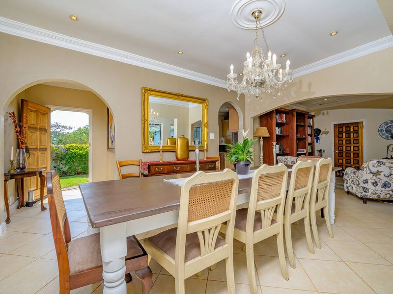 Spacious dining room featuring elegant crown molding, a classic crystal chandelier, tiled flooring, and arched access to the garden and adjacent living areas.
