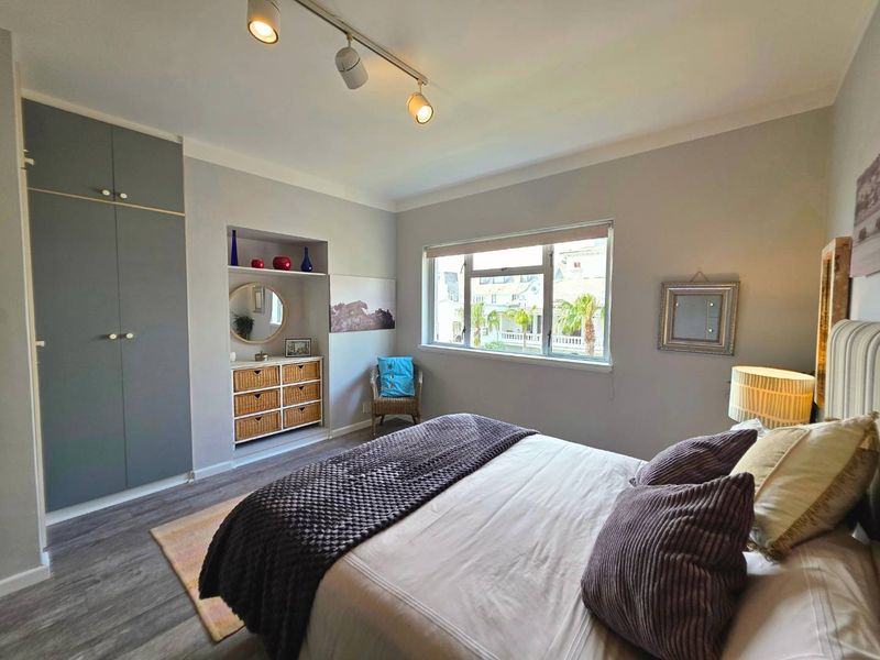 A well-maintained bedroom featuring built-in wardrobes, recessed shelving, modern track lighting, and durable laminate flooring with a pleasant exterior view.