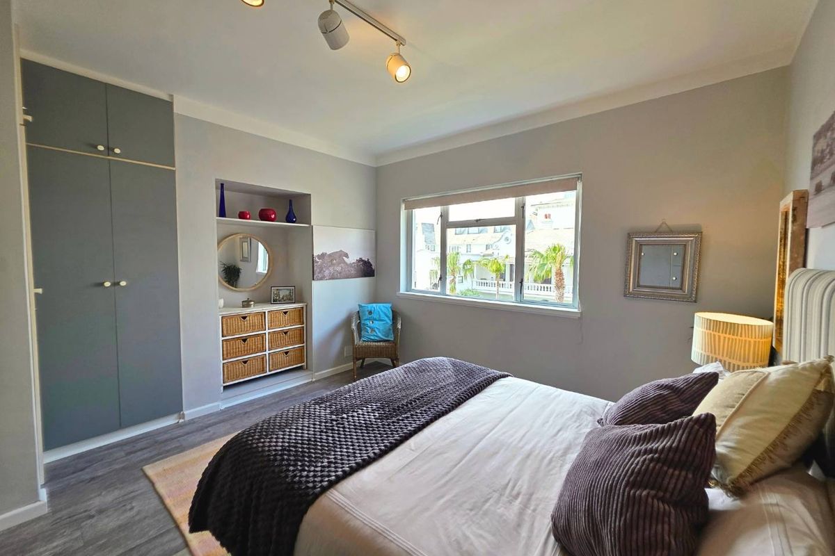 A well-maintained bedroom featuring built-in wardrobes, recessed shelving, modern track lighting, and durable laminate flooring with a pleasant exterior view.