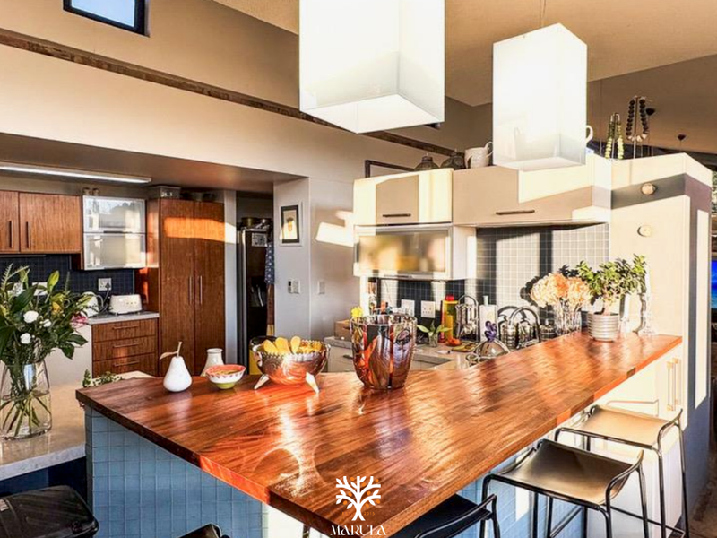 A modern kitchen featuring a prominent wooden breakfast bar, tiled backsplash, and ample built-in cabinetry with stylish pendant lighting.