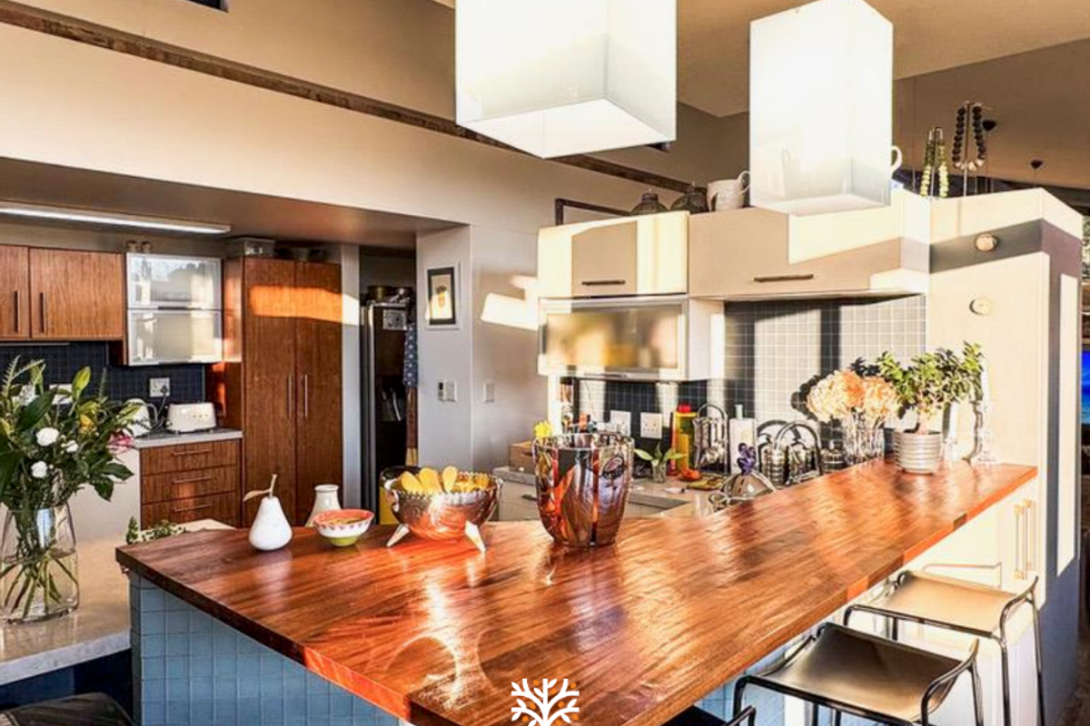 A modern kitchen featuring a prominent wooden breakfast bar, tiled backsplash, and ample built-in cabinetry with stylish pendant lighting.