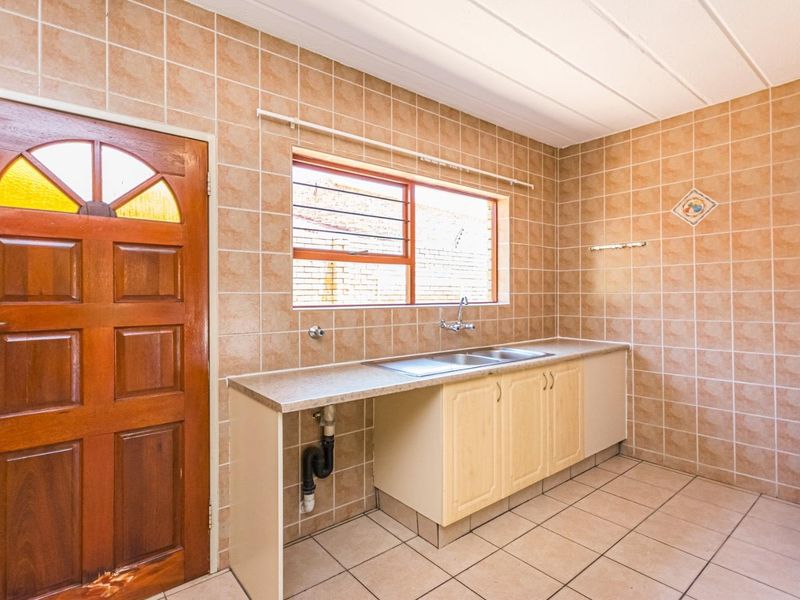 A functional laundry room featuring tiled walls and flooring, built-in cabinetry with a stainless steel sink, and direct access to the exterior.