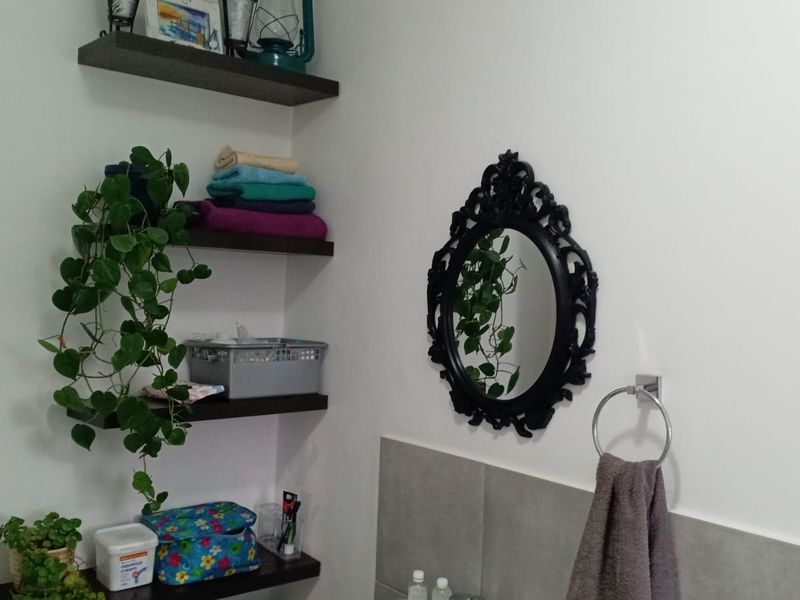 A bathroom corner featuring built-in dark wood shelving, a tiled splashback, and a wall-mounted towel ring.