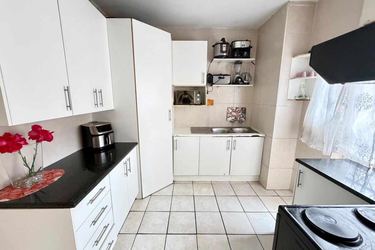 A functional kitchen featuring white cabinetry, dark granite countertops, tiled flooring, and a double-basin stainless steel sink.