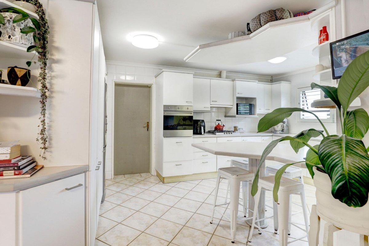 A functional kitchen featuring white cabinetry, built-in oven, gas hob, and a central breakfast bar with tiled flooring.