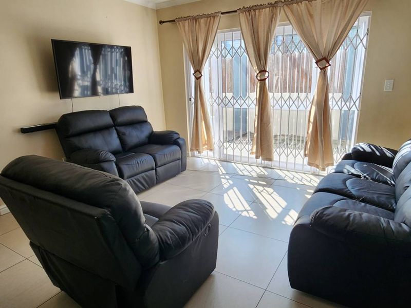 A living room featuring tiled flooring and a sliding glass door with a security gate, providing access to the exterior.