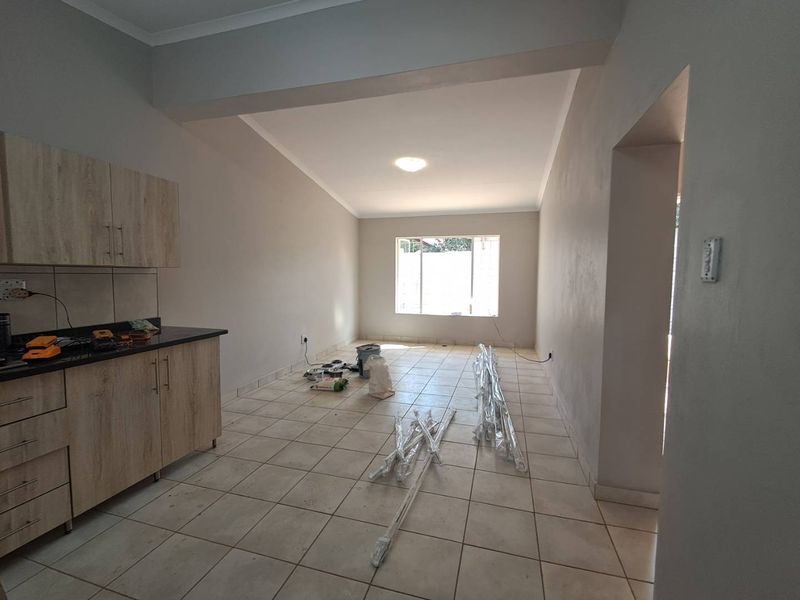 An open-plan living and kitchen area featuring neutral walls, tiled flooring, and modern wood-finish cabinetry, currently in a vacant state.