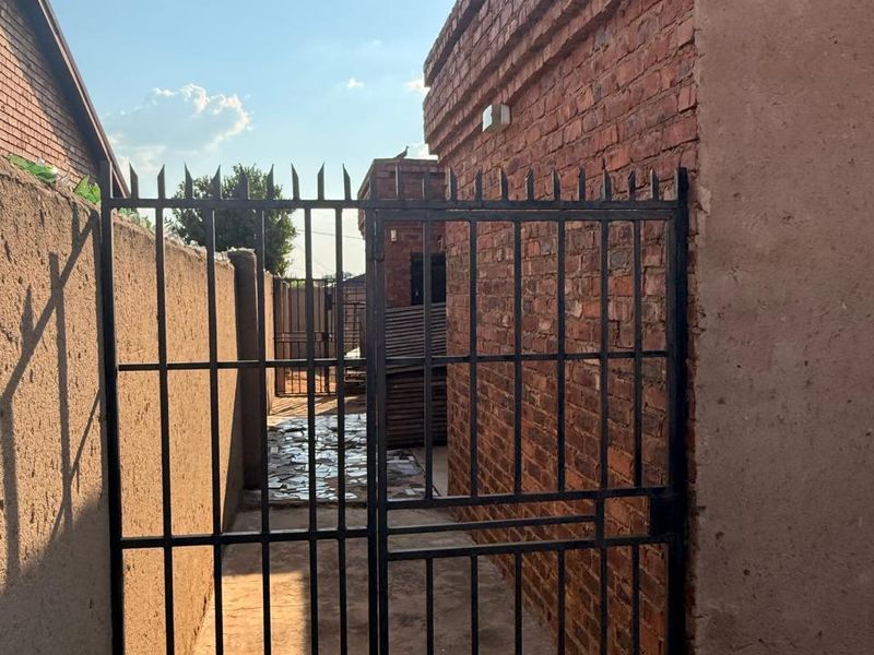 A narrow side passage featuring exposed brick walls, a metal security gate, and paved flooring leading to the rear of the property.