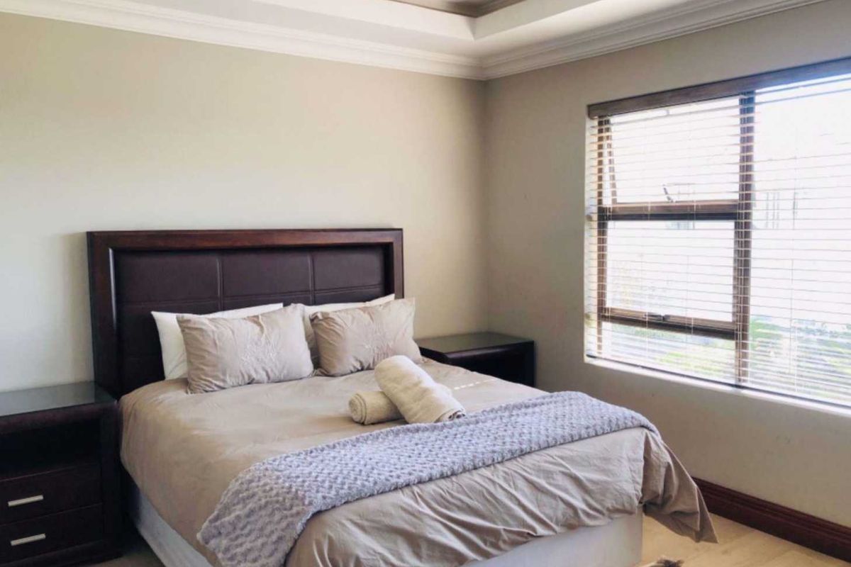 A well-maintained bedroom featuring a tray ceiling, neutral wall tones, and large windows with fitted blinds, providing a bright and comfortable living space.