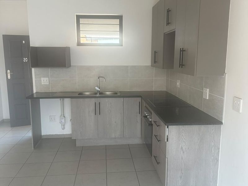 Modern kitchen featuring grey built-in cabinetry, dark stone countertops, stainless steel sink, built-in oven, and neutral tiled flooring.