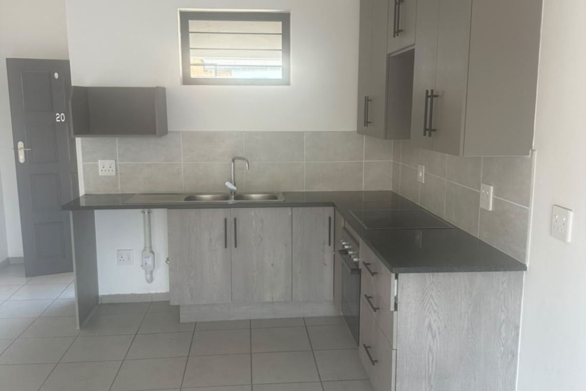 Modern kitchen featuring grey built-in cabinetry, dark stone countertops, stainless steel sink, built-in oven, and neutral tiled flooring.