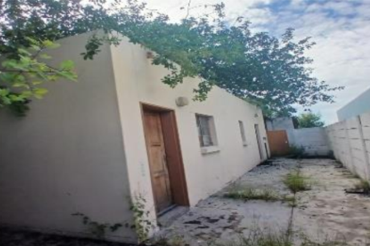 Rear exterior view of the industrial property featuring a paved yard area enclosed by a concrete boundary wall with visible signs of weathering.