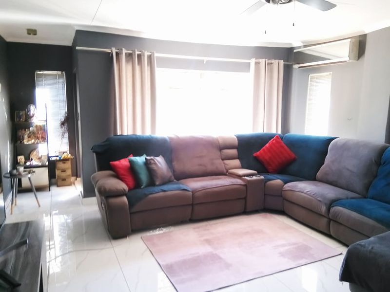 A comfortable living room featuring tiled flooring, a ceiling fan, and an integrated air conditioning unit, providing a functional and well-maintained space.