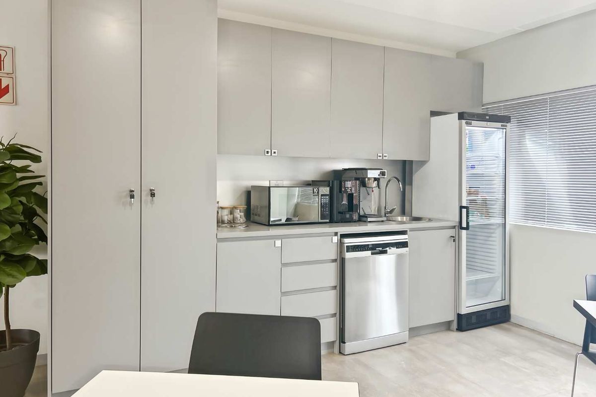 A modern office kitchenette featuring sleek grey cabinetry, a stainless steel dishwasher, integrated sink, and ample storage space.