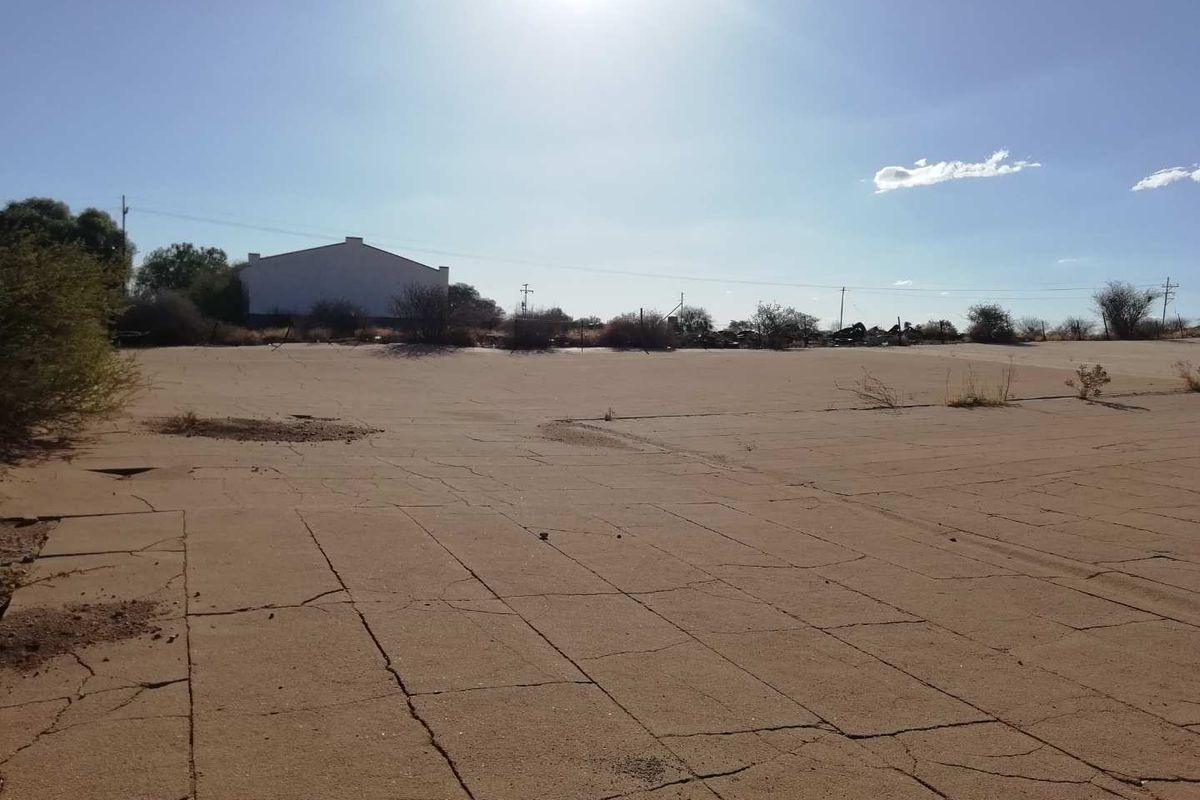 A wide view of a vacant agricultural plot featuring a large, cracked concrete slab area and surrounding natural landscape.