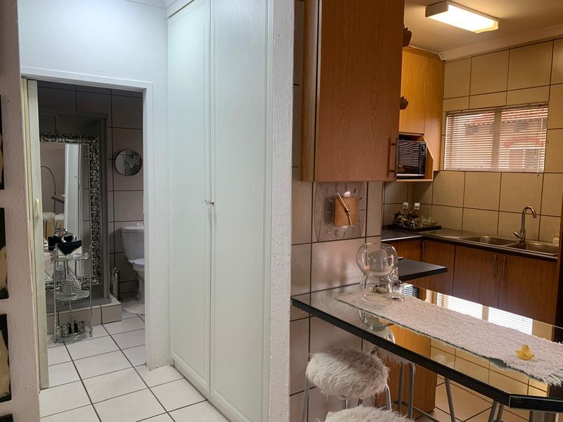 A functional kitchen featuring wood-finish cabinetry, tiled backsplash, and a breakfast bar, with an adjacent view into a tiled bathroom area.