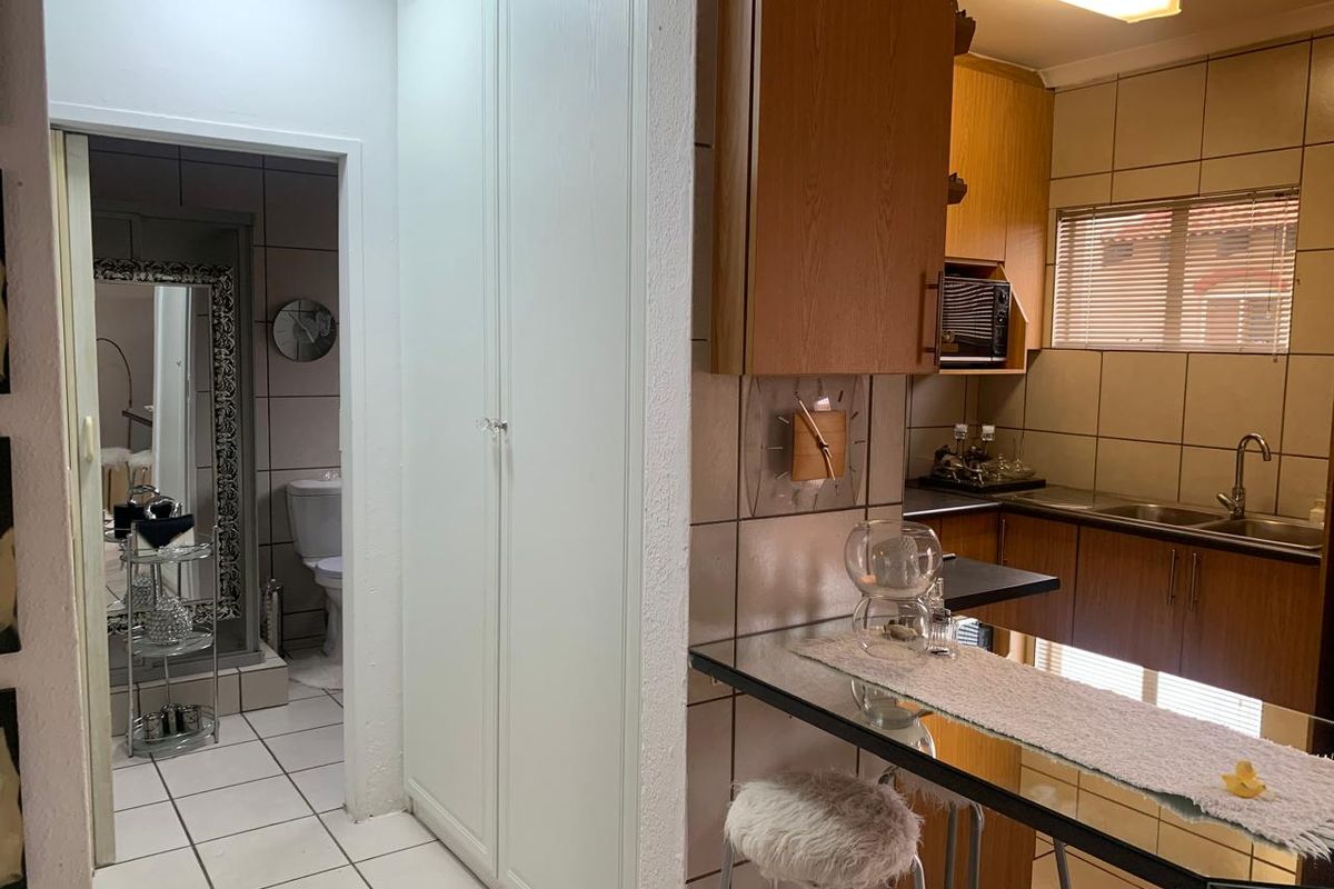 A functional kitchen featuring wood-finish cabinetry, tiled backsplash, and a breakfast bar, with an adjacent view into a tiled bathroom area.