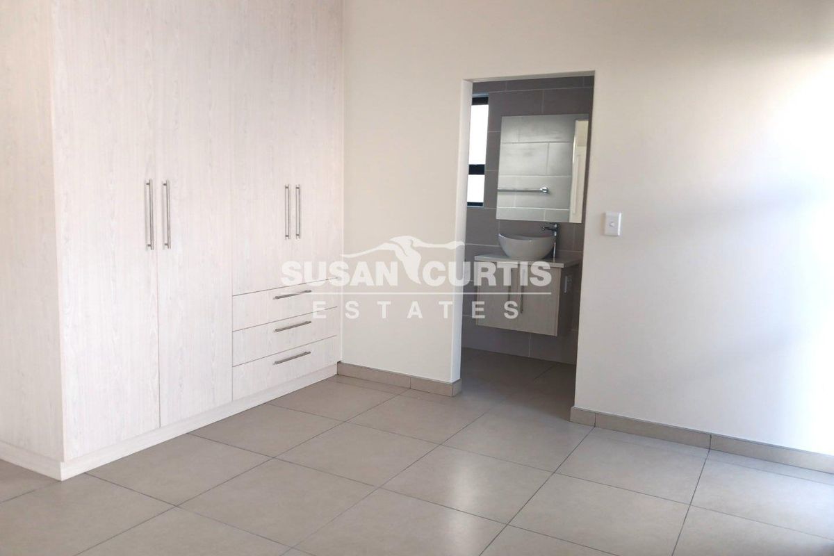 A bright bedroom featuring built-in wardrobes with light wood-grain finish, tiled flooring, and an en-suite bathroom access.