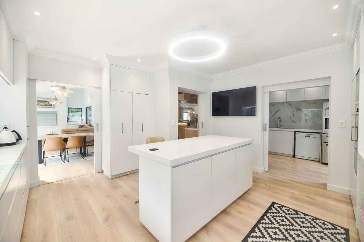 Modern, bright kitchen featuring a central island, sleek white cabinetry, and seamless flow into the adjacent scullery and dining area.