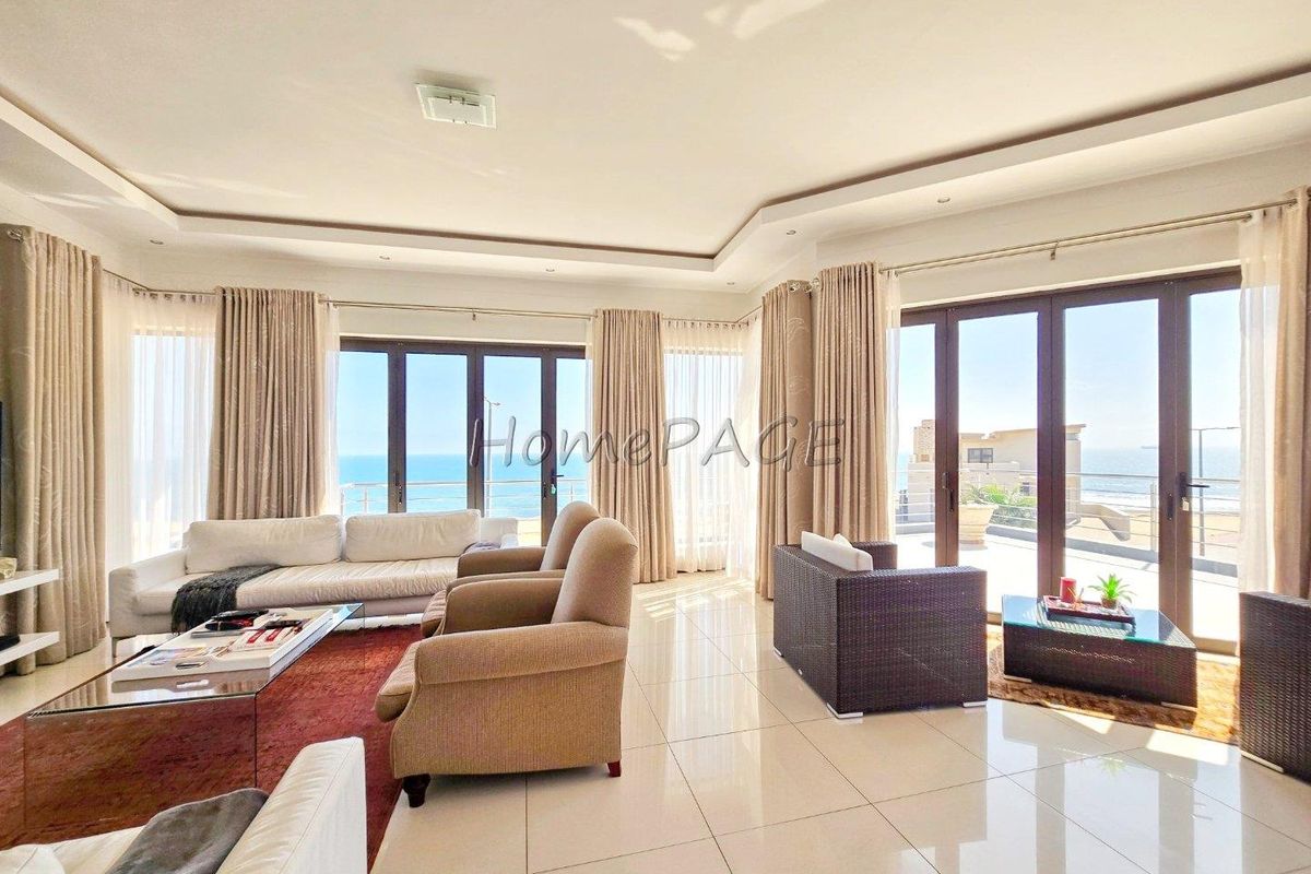 Spacious living area featuring large glass sliding doors that open onto a balcony with expansive ocean views and polished tile flooring.