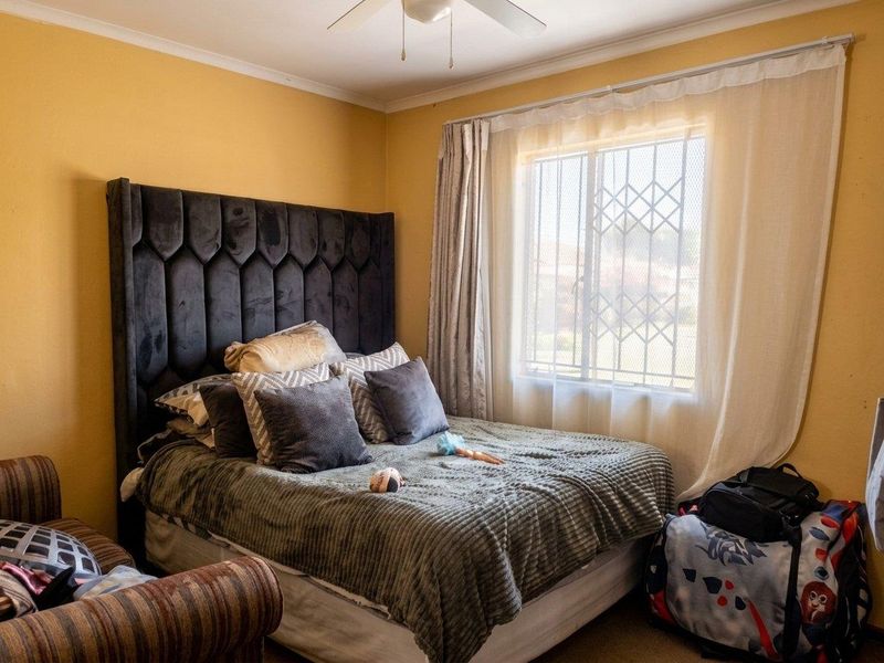 A bedroom featuring a ceiling fan and a window fitted with a security gate, providing natural light and ventilation.