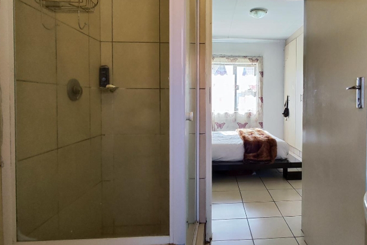 A view from a bathroom looking into a bedroom, featuring tiled flooring and a shower enclosure with built-in fixtures.